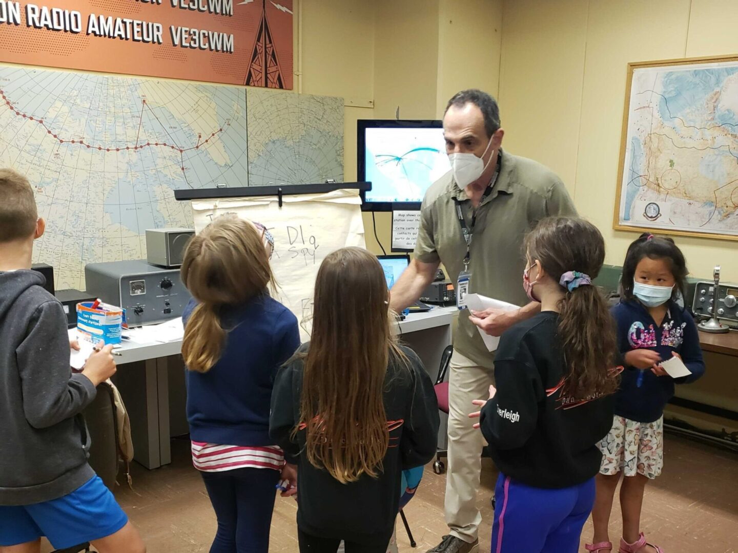 A man explains radio equipment to children in a classroom.