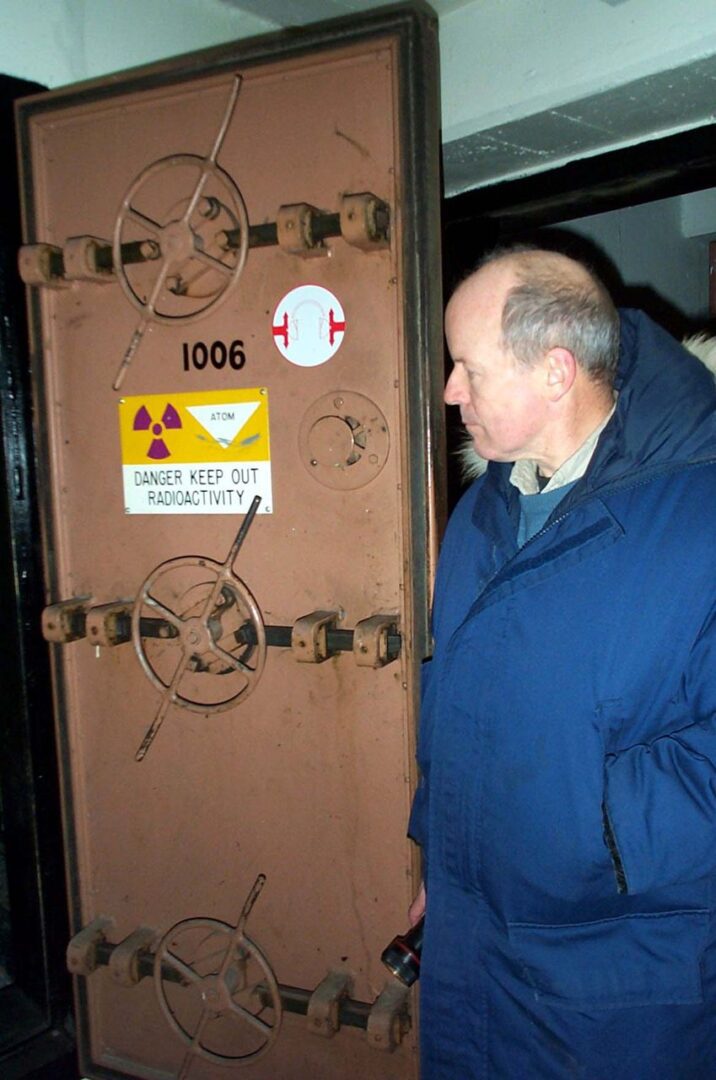 Man inspecting a heavy metal door with warning signs.