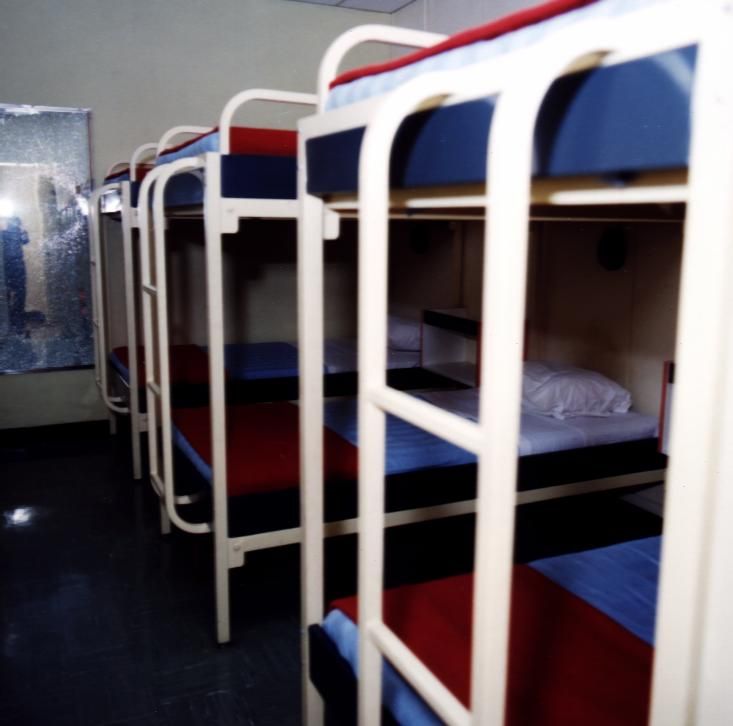 A row of empty metal bunk beds with blue mattresses in a room.