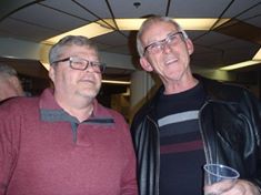 Two older men smiling indoors under ceiling lights.