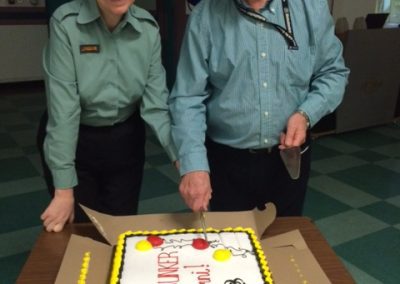 Two people in uniform cutting a decorated cake.