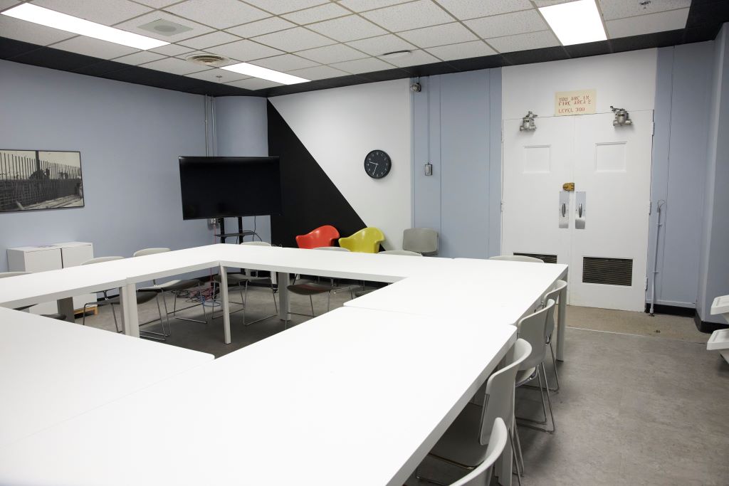 Modern conference room with white tables and chairs arranged in a square.
