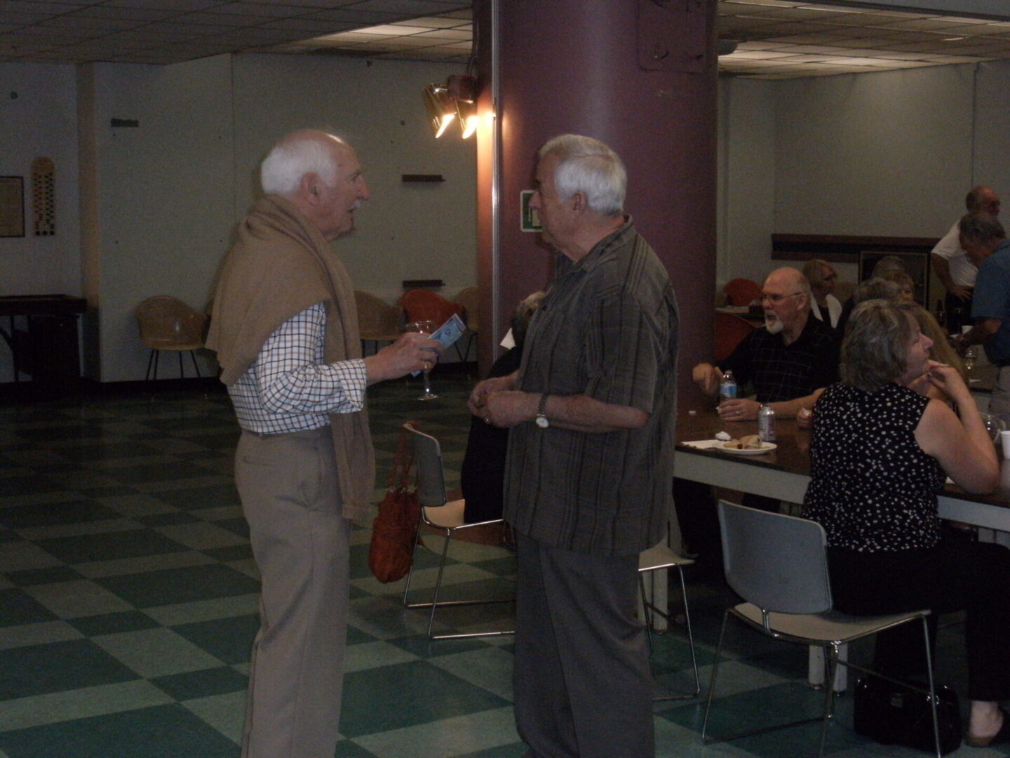 Two elderly men chatting in a casual indoor setting.