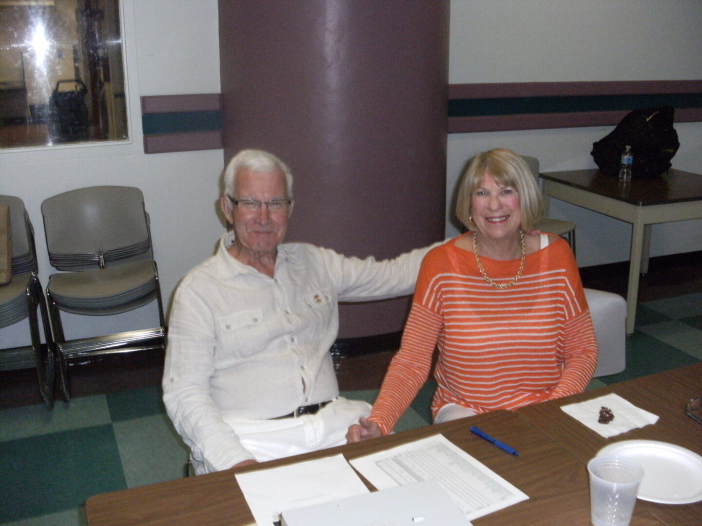 An elderly man and a middle-aged woman seated at a table with papers.