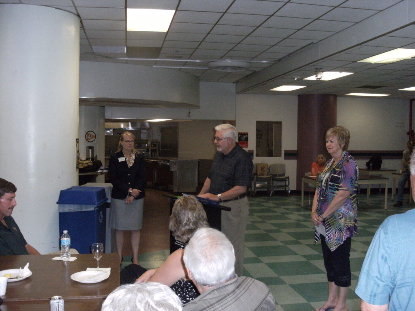 Three people standing at the front of a room addressing seated attendees.