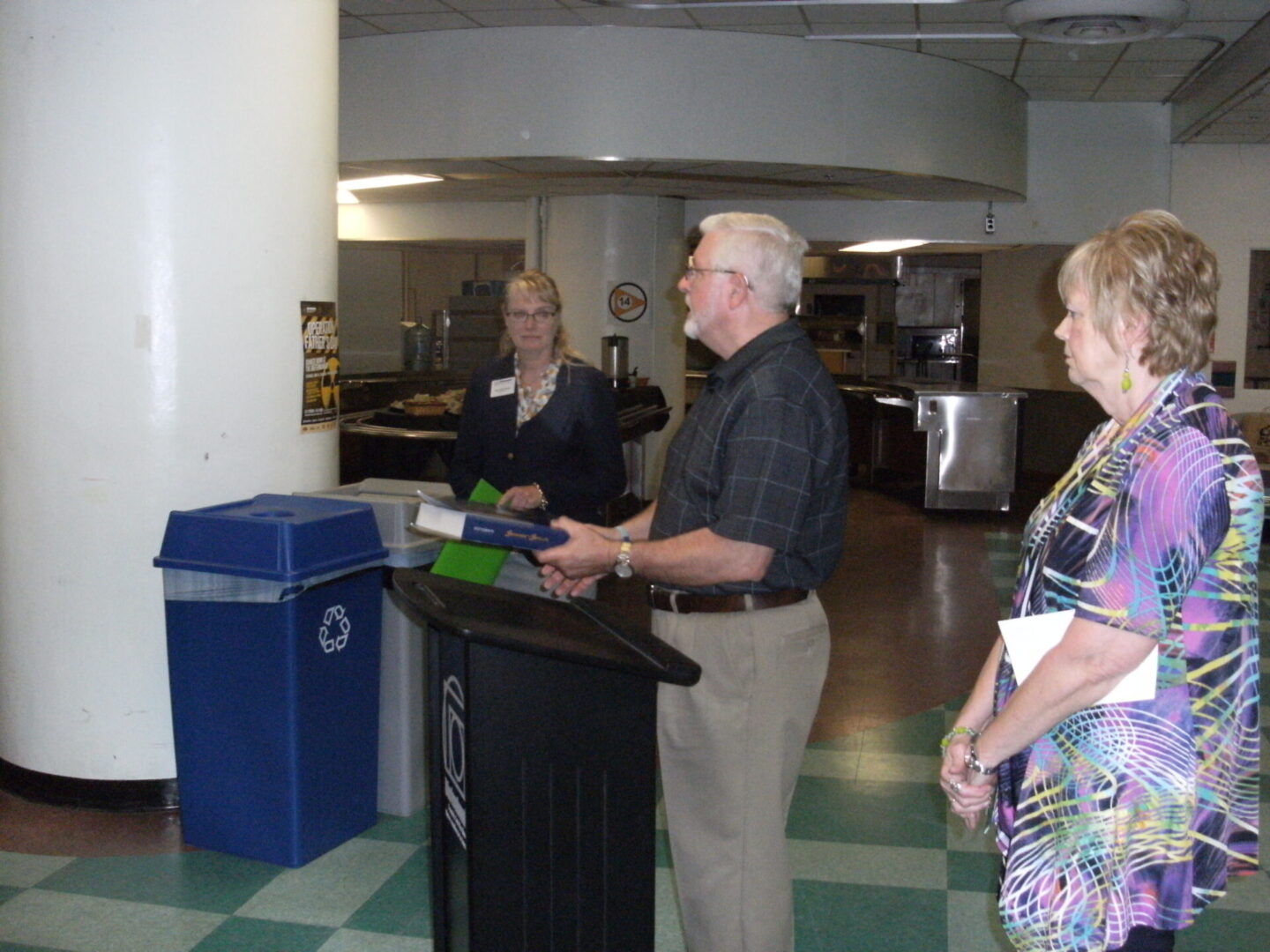 A man speaking at a podium in an indoor setting with a few listeners.