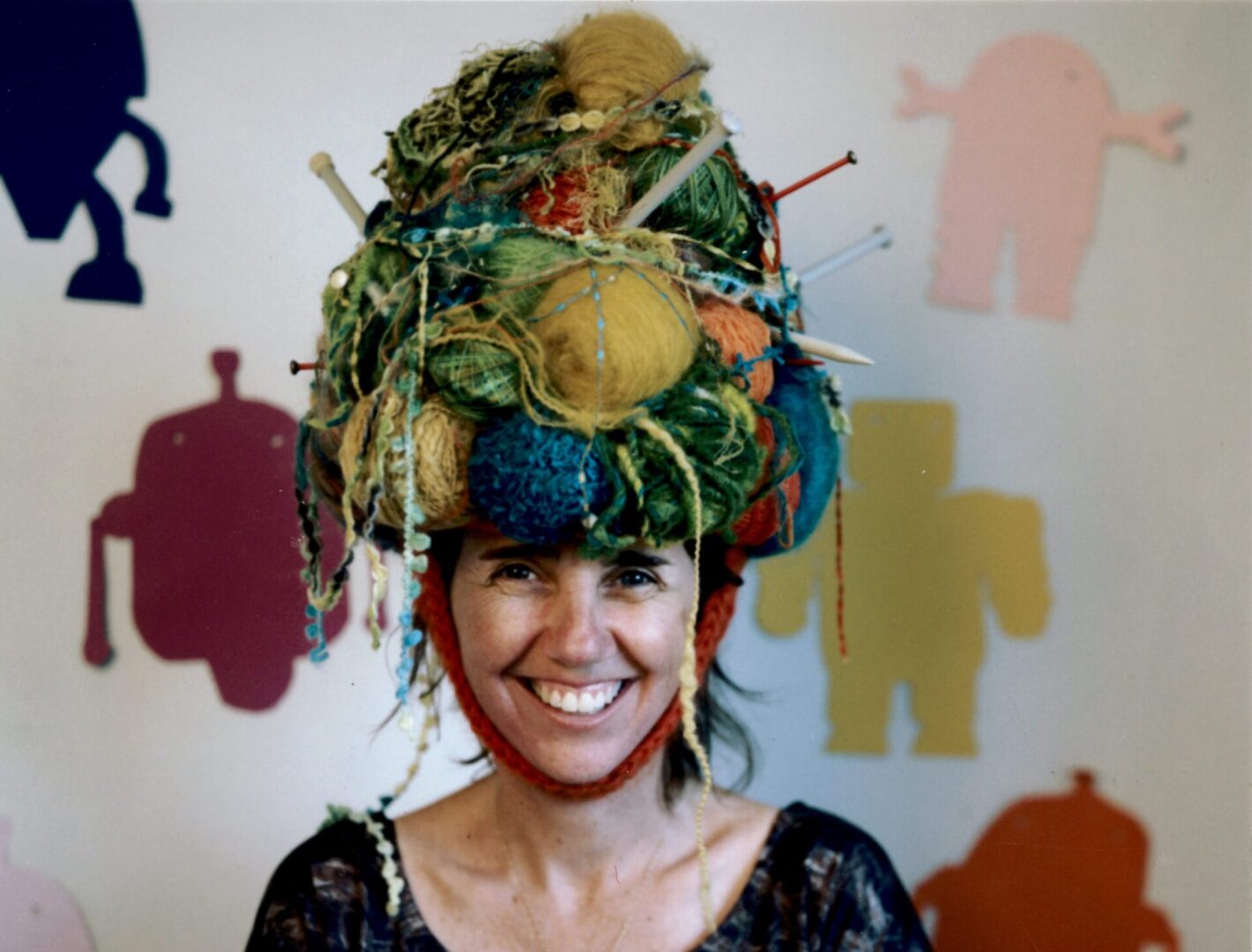 Woman smiling with a colorful, elaborate headpiece made of various objects.