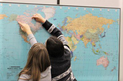 Two people marking locations on a world map.