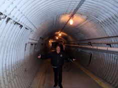 Person standing in a dimly lit tunnel with exposed pipes.