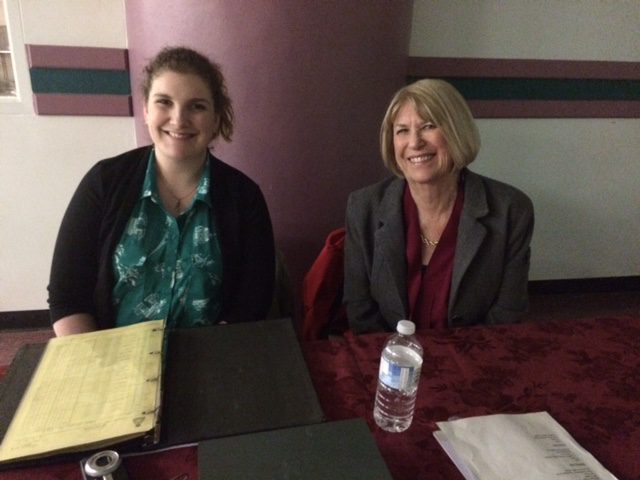 Two women sitting at a table with a water bottle and menu.