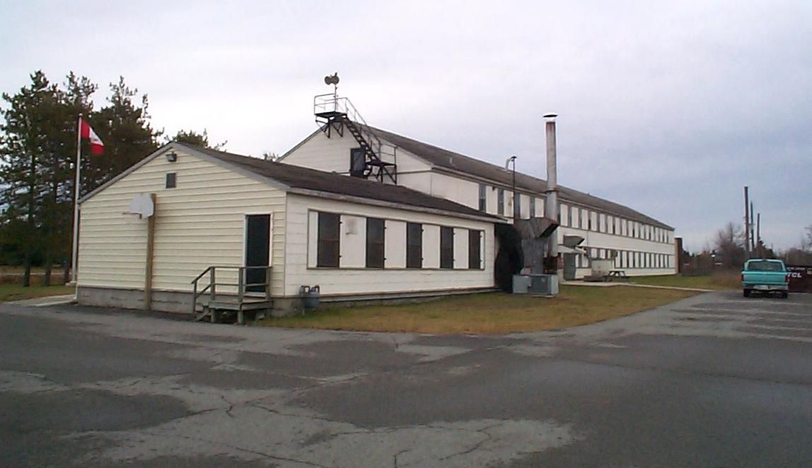 A long, white industrial building with multiple windows and a chimney.