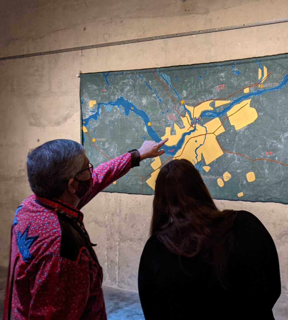 Two people examining a detailed map on a wall inside a dimly lit room.