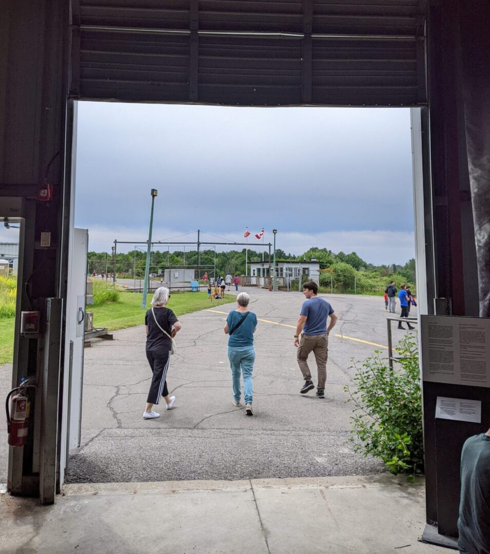 Three people stand outside a large open doorway looking at a sports field.