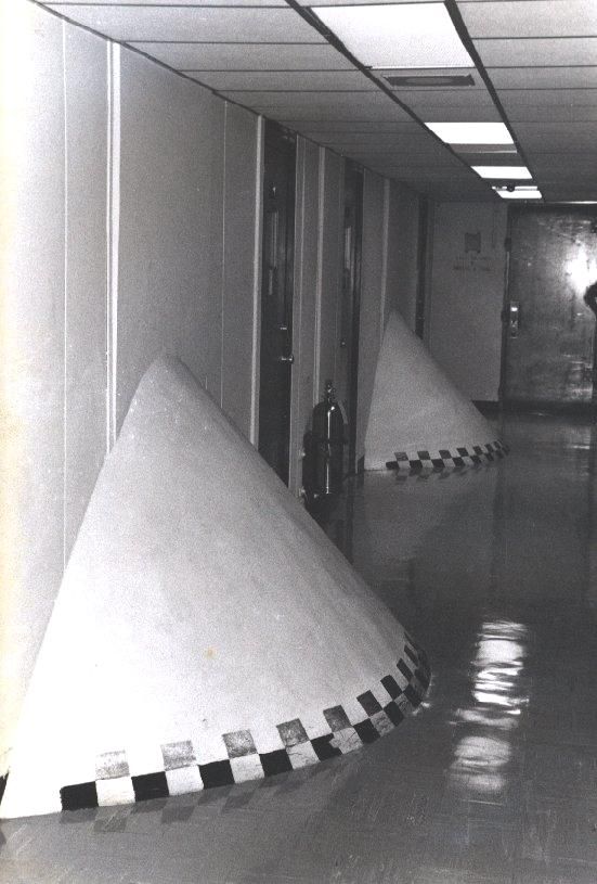 Large conical structures lined up in a hallway with reflective floors.