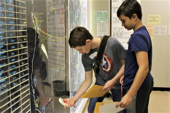 Two boys are playing with a hand dryer in a restroom.