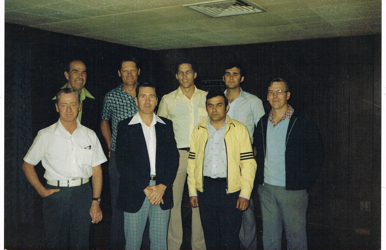 A group of eight men posing indoors in casual and semi-formal attire.