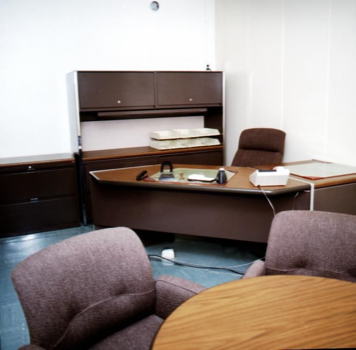 A vintage office with a wooden desk, brown chairs, and a round meeting table.