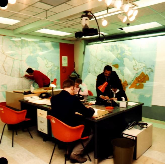 People working in a vintage office with one person sitting on a high shelf.