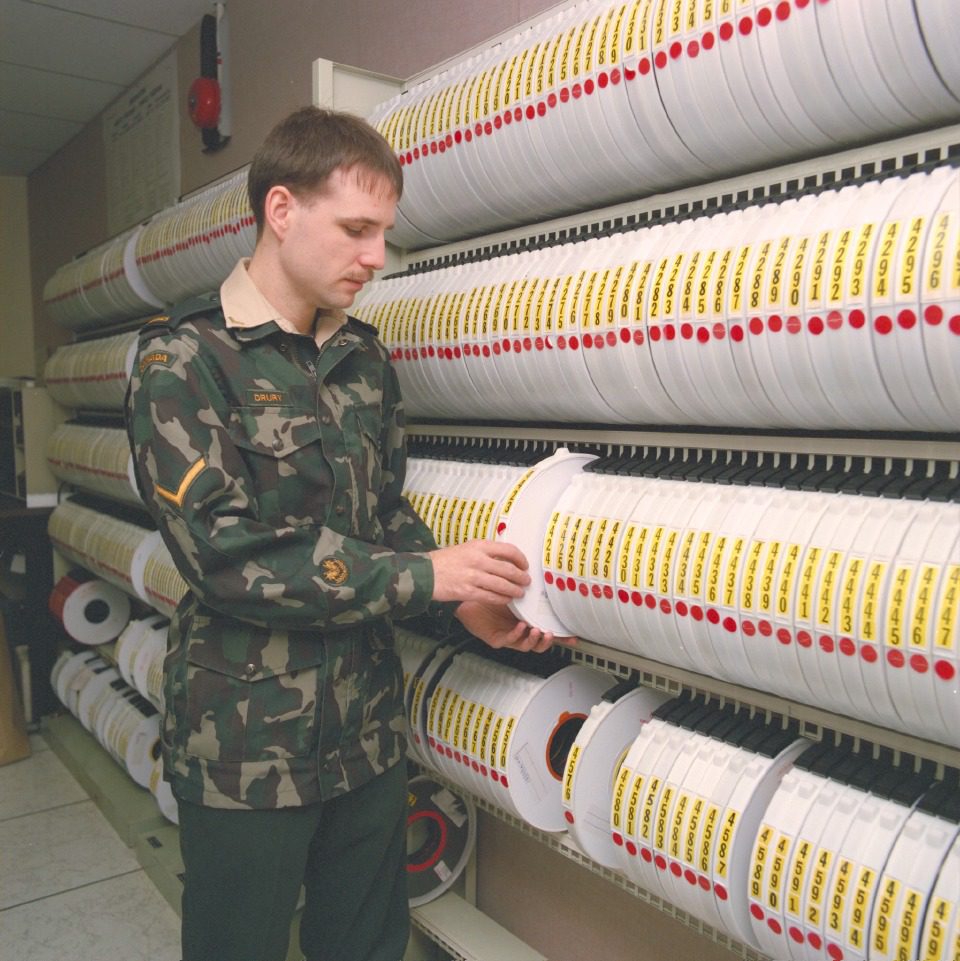 A man in camouflage uniform checking records on shelves.