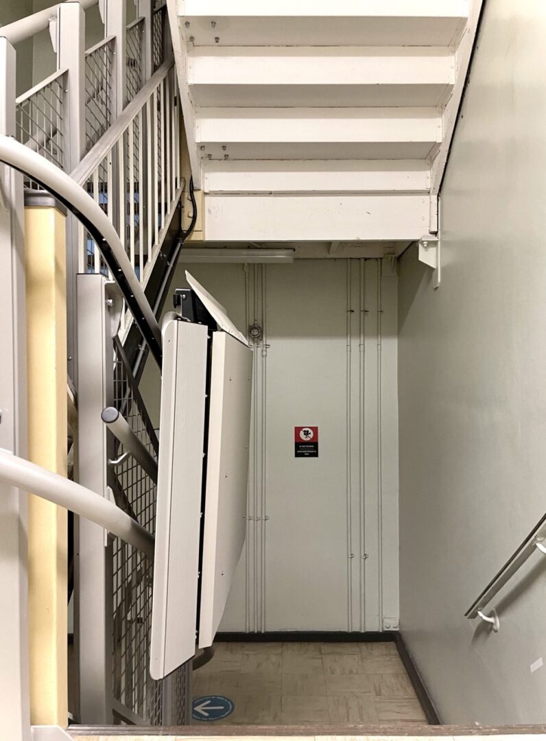 Elevator doors at the bottom of a stairwell with safety rails and warning sign.