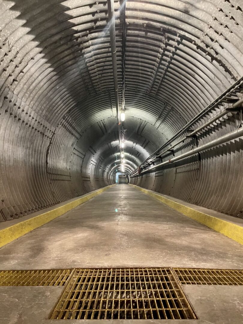 Empty industrial tunnel with curved metal walls and overhead lighting.