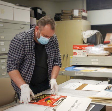 Man wearing a mask and gloves organizing papers on a table.