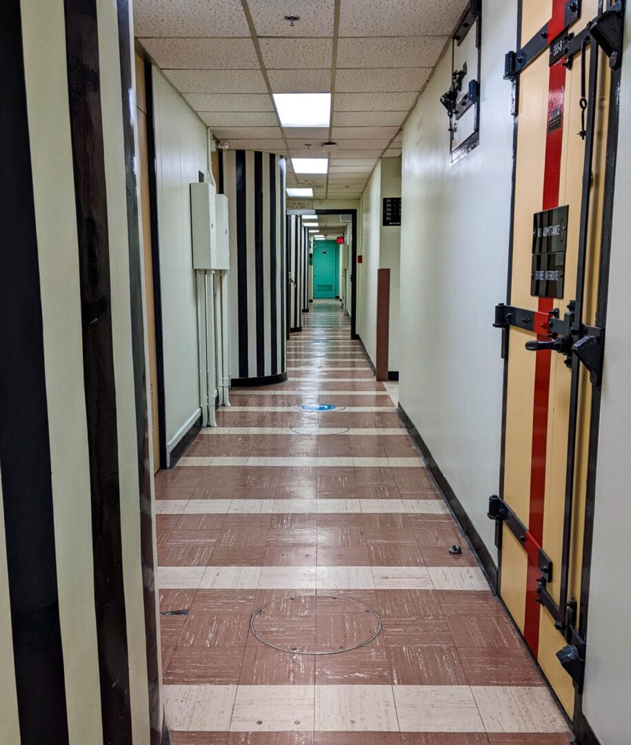 Long hospital corridor with multiple doors and tiled floor.