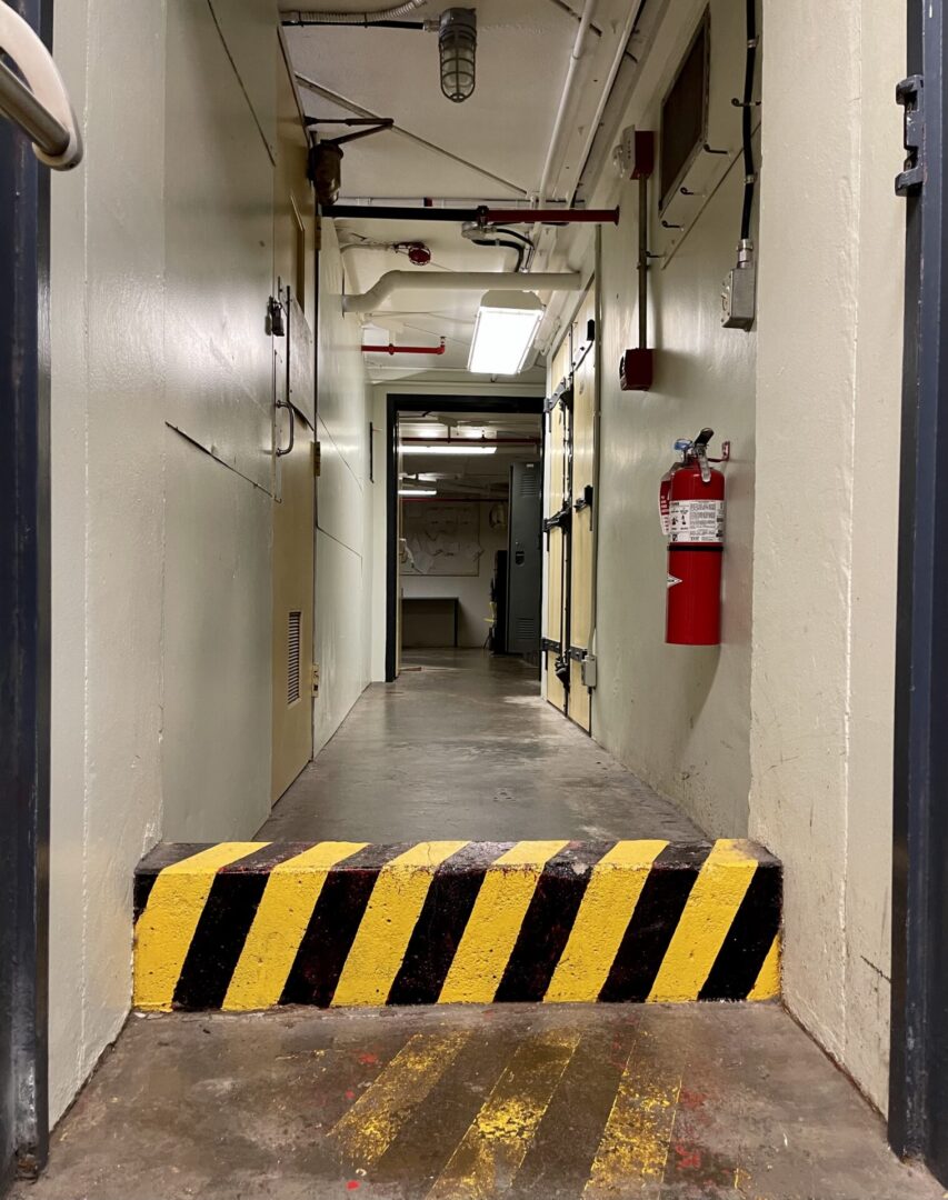 A narrow industrial hallway with a striped barrier and fire extinguisher.
