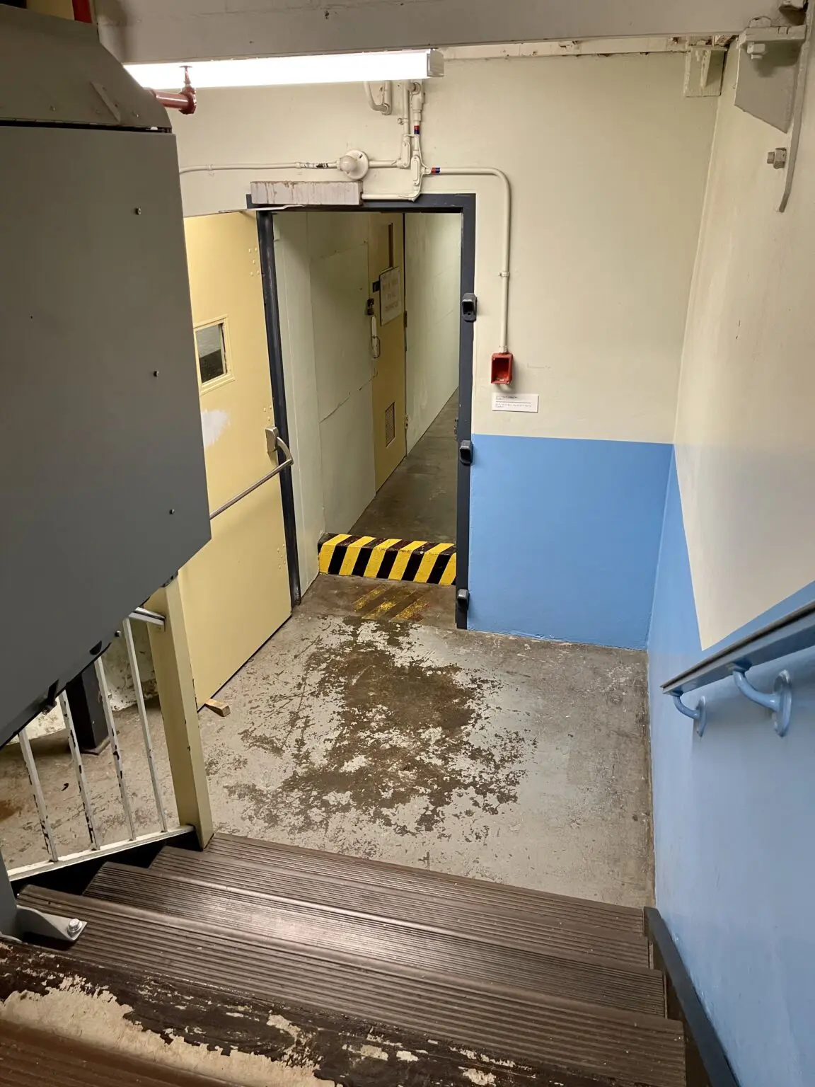 A stairwell leading to a closed door with caution tape on the floor.