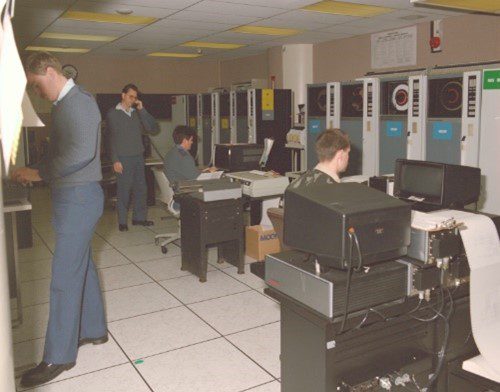 A busy computer lab with people working on vintage mainframe computers.