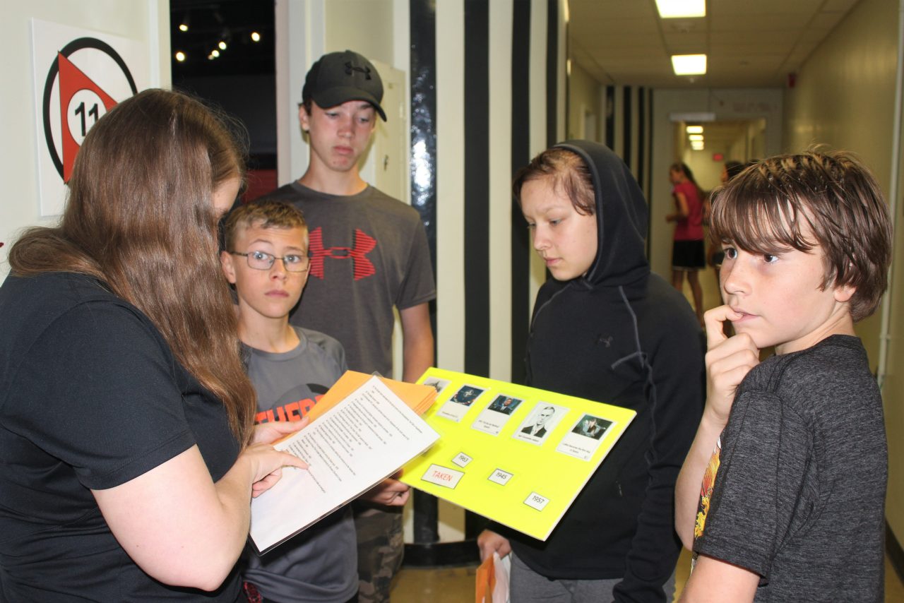 A group of young people reviewing a yellow folder in a hallway.
