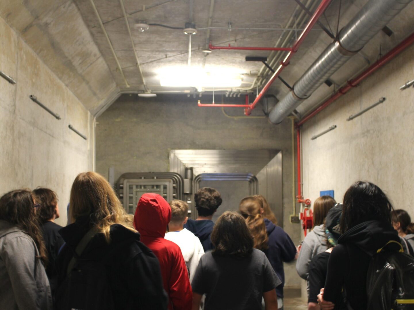 People walking through an industrial hallway with exposed pipes.