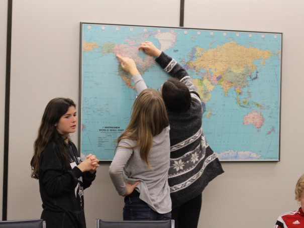 Three people placing sticky notes on a world map on the wall.
