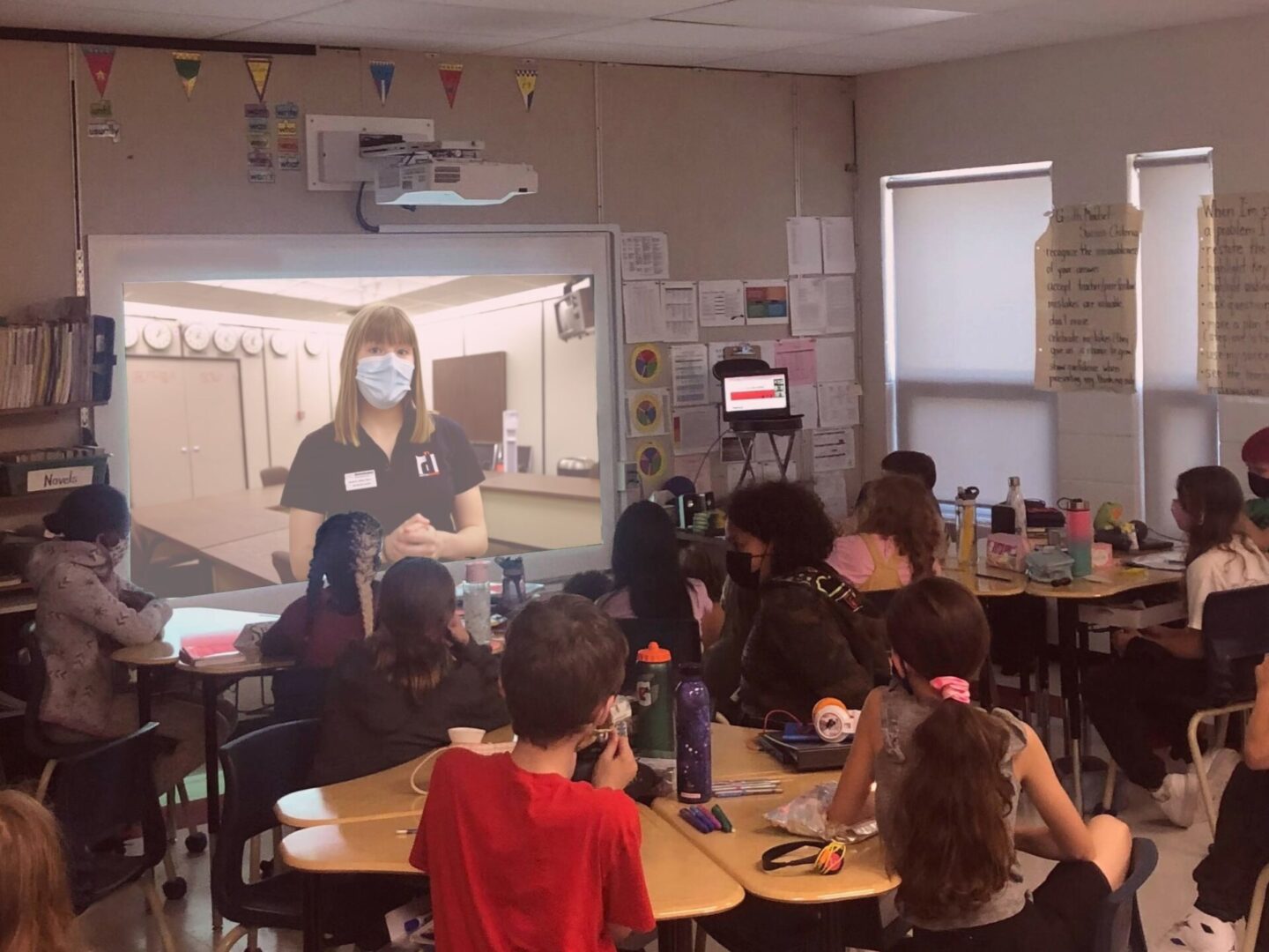 Teacher wearing a mask instructing a classroom of attentive students.
