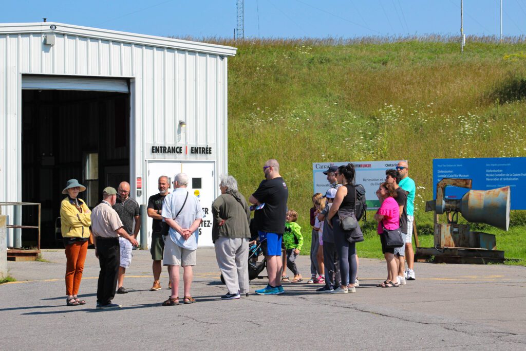 A volunteer engages with a group of visitors out front of the museum.