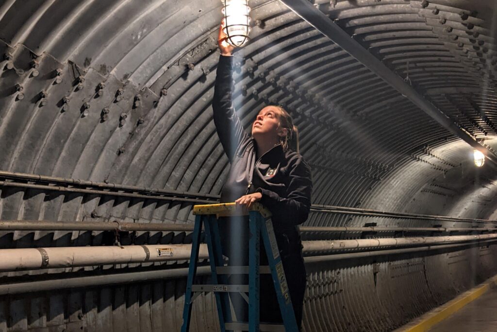 A person stands on a ladder changing a lightbulb in the Diefenbunker's Blast Tunnel.