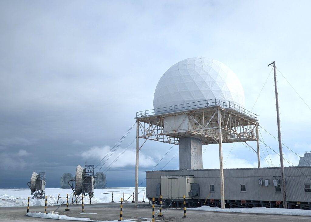 A large white dome sits on top of a low building, in a snow covered area.