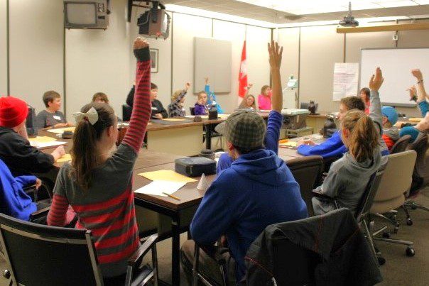 Kids raising hands in a meeting room during a classroom program.