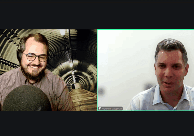 Two men smiling during a video call, one with headphones and the other with a white shirt.