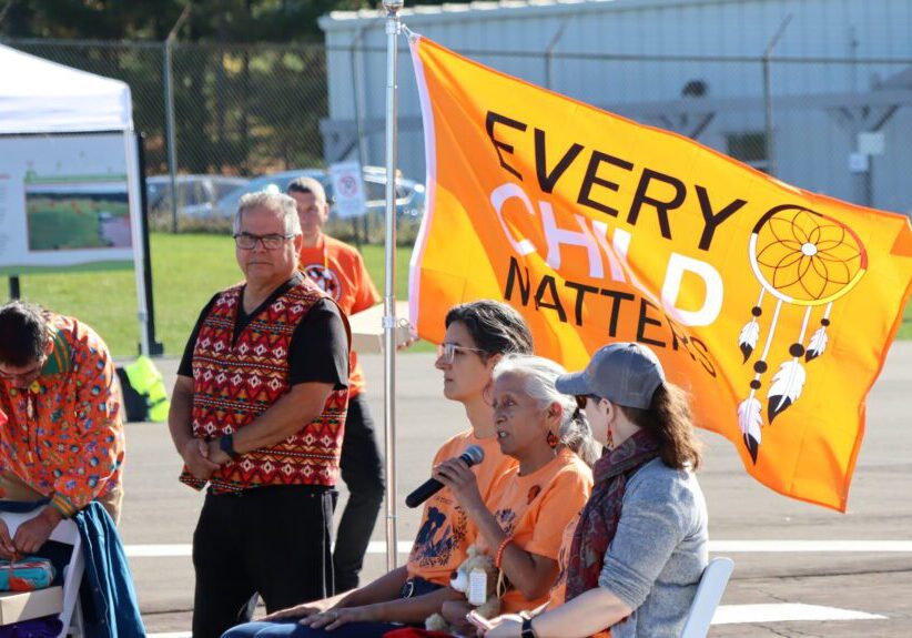 People gathered outdoors with a bright yellow banner reading 'Every Child Matters'.